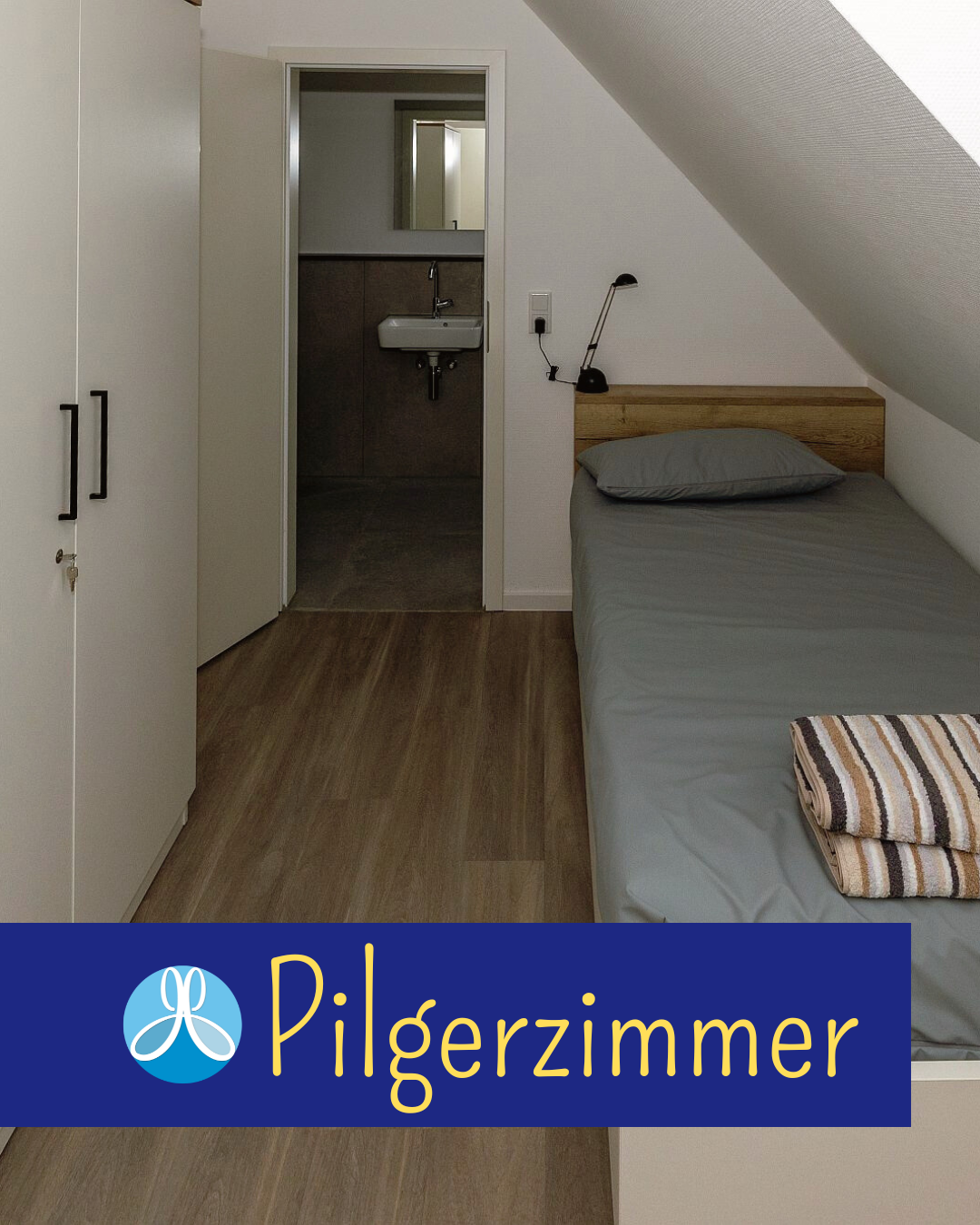 Ein Bild vom Pilgerzimmer - Bett, Schrank, Leuchte und eine offene Tür, die ins Bad führt. Darunter das Logo der Pfarrei St. Johannes Baptist und das Wort Pilgerzimmer.